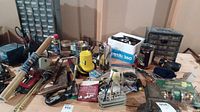 Wide view of workbench with assorted tools, clamps, fasteners, and workshop supplies arranged on surface.