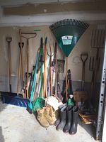 Full view of yard tools against wall including rakes, shovels, boots and basket of garden tools