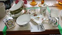 Display of fine china and serveware items including creamers, bowls, gravy boat, a clock, and floral plates.