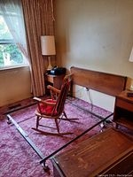 Full view of the queen size bed frame and wooden headboard in a room with carpet and a rocking chair.