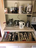 Photo of kitchen countertop with blender, electric kettle, saucepans, glass baking trays, and utensils in drawer.