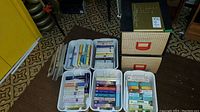 Overview of four white plastic filing boxes filled with various novels and a beige two-drawer cardboard filing cabinet with orange handles