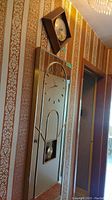 Side and angled views of the tall mirrored wall clock with clock face, gold hour markers, and visible pendulum, mounted on wallpapered wall.
