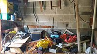 Tools, cords, power cutters, and hedge trimmers arranged on a table and shelf including orange/red power cutters and several extension cords