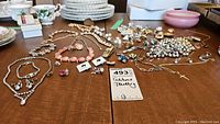 Wide view of assorted costume jewelry including necklaces, bracelets, brooches on a wooden surface with plates in background