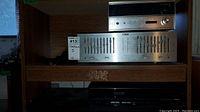 Wood shelf with Audio Reflex EQ-2 stereo equalizer on bottom and Sansui RA-700 reverberation amplifier on top, plus black video device below shelf.