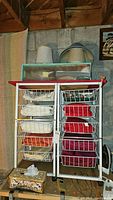Two wire storage carts with multiple baskets filled with folded fabrics and towels, lampshades on top, clothes iron and tissue box positioned nearby.