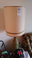 Full view of one lamp showing the tall cylindrical cream shade with gold trim and green ceramic base with textured decoration.