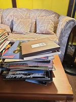 Stack of various vinyl records on wooden table next to couch.