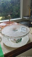 Glass cake plate with handle and amber-colored two-tier glass plate in daylight by window