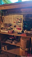 Wide shot of sewing supplies arranged on wooden shelf against concrete wall, including some plastic storage baskets and shelving units.