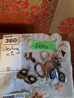 Photo showing seven pieces of sterling silver jewelry on fabric background including four pairs of earrings, a ring, and a chain with pendant.