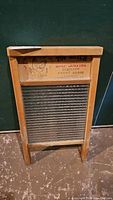 Wooden framed vintage washboard with metal scrubbing surface standing upright on the floor against a wall.