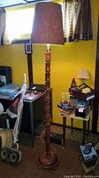 Full view of the wood floor lamp standing in a room with a cylindrical brown fabric lampshade and segmented wood column.