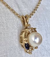 Close front view of pendant showing pearl, sapphire and diamond accents and bail on chain.