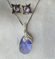Pair of star-shaped sterling silver earrings with oval amethyst stones and sterling silver pendant necklace with pear-shaped amethyst and rhinestone decoration on chain.