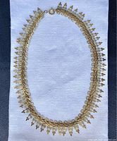 Full view of brass necklace laid flat on fabric, showing entire chain and attached decorative elements.