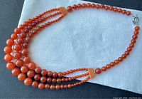 Triple strand carnelian necklace laid flat on white and dark fabric backgrounds to show bead graduation and clasp.