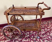 Side view showing two-tier carved lattice shelves, large rear wheels and handles, with custom inset glass top visible.
