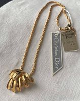 Full view of Christian Dior gold-tone necklace showing twisted rope chain, feather pendant, and attached original tags.