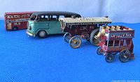 Four vintage toy vehicles arranged in a row on blue fabric background, front to back: small red vintage bus, open carriage, turquoise van, red double decker bus.