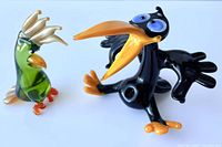Front view of green parrot and black crow glass figurines together on a white surface.