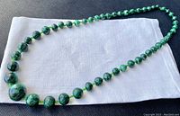 Full view of the necklace laid flat showing graduated malachite beads on a white cloth.