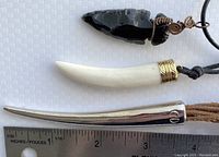 Three necklaces laid flat with ruler for scale. Includes knapped black obsidian arrowhead pendant, white horn-shaped pendant with gold-tone cap, and silver-tone horn pendant.