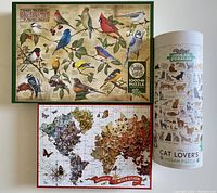 Full view of three puzzles: Cobble Hill bird puzzle, Galison butterfly migration puzzle, Ridleys cat puzzle in cylinder