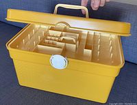 Top view of open yellow plastic sewing box showing multiple internal compartments and a central removable tray
