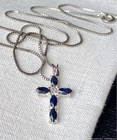 Close-up of the necklace showing the cross pendant with blue marquise-shaped gemstones.
