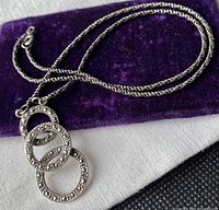 Sterling silver necklace laid on purple fabric pouch showing the chain and marcasite three-ring pendant