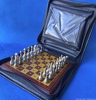 Travel chess set opened in black zippered case with metal chess pieces on wooden board with holes