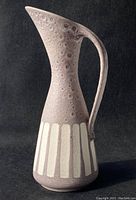 Front and side view of ceramic vase showing tall, curved handle and vertical white stripes on lilac speckled body.