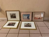 Five framed prints/photos arranged on tiled floor against wall, showing variety of nature scenes.