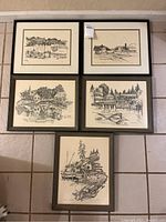 Five framed pen and ink destination prints laid out on tile floor, showing variety of scenes with water, buildings, and boats.