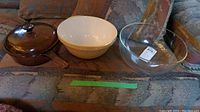 Full view of the three items: brown Corning Vision saucepan with lid, cream pottery mixing bowl, clear glass bowl.