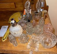 Assorted vintage and empty perfume bottles, cologne, lotion, and decorative glass items on wooden table, various shapes and sizes, some without stoppers.