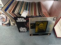 Overview of vintage vinyl records stacked together showing various album spines and some covers, including Paul Simon and Madama Butterfly.