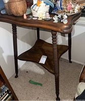 Front-side view showing table with twisted carved legs, dark wood grain top with curved edges, and lower uniquely shaped shelf.
