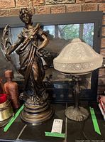 Photo showing the metal statue 'Victrix' next to the glass globe lamp on a mantle in front of a fireplace.