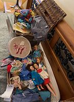 Vintage dolls posed with doll clothes and accessories in wicker baskets and on carpet.