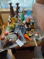 Overview of the kitchen collectibles including glass vases, figurines, novelty salt and pepper shakers, glass trays, and other vintage tableware items on a dark wooden table