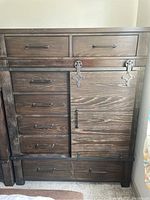 Front view of dark stained wood barn style armoire with drawers and sliding door showing metal hardware.