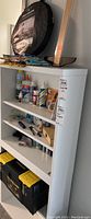 Photo taken showing the shelving unit with multiple art supplies, adhesives, tapes, and glues visible on shelves with Stanley toolbox on the floor