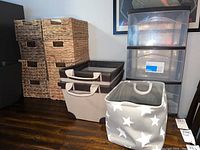 Photo showing four woven baskets stacked on the left, two dark brown cloth bins, two light-colored star-patterned bins on right and medium 3-drawer plastic storage cart at back right.