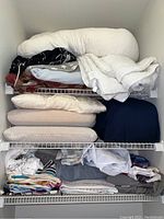 Full view of three shelves stocked with linens including comforters, towels, and sheets.