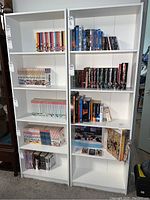 Front view of two white pressed wood bookcases filled with books and DVDs (contents not included).