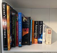 Shelf with eleven assorted reference and general interest books including Nature's Great Events, web design, the raptor almanac, astronomy, science, minerals and gemstones, cyclopedia encyclopedia, among others.