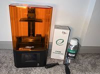 Creality 3D resin printer with orange translucent cover, eSUN resin bottle and resin scraper tool arranged side by side.